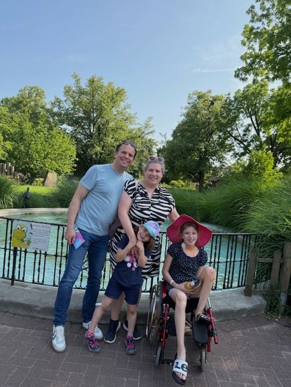 Zu sehen ist Sophia in ihrem Rollstuhl mit ihrer Familie.  Insgesamt zu 4. auf dem Bild.